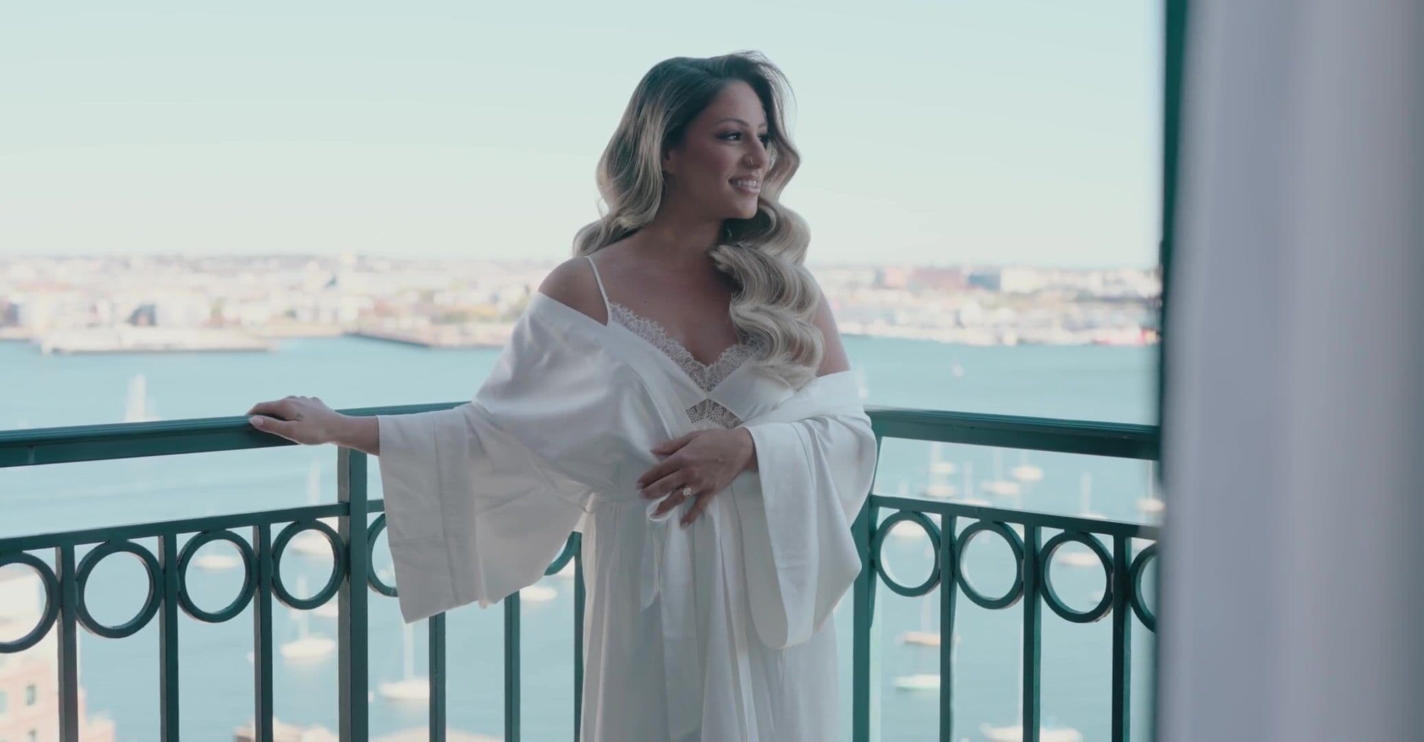 A bride looking out over Boston Harbor from a hotel balcony at Rowes Wharf while getting ready