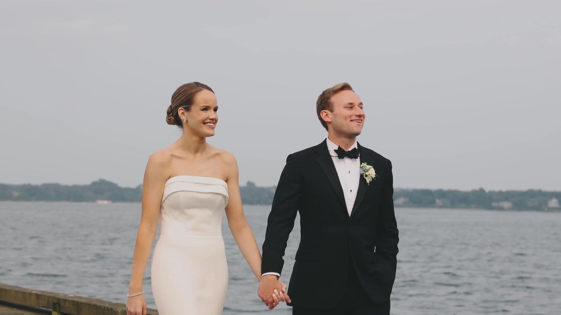 A bride and groom walking hand in hand on a dock on the Sakonnet River at dusk