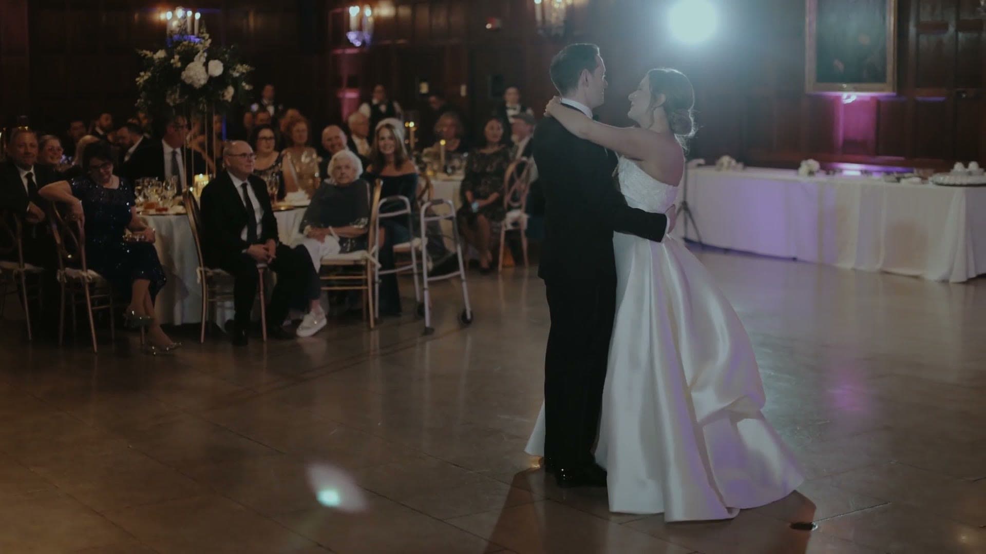 A bride and groom sharing their first dance in the wood-panelled hall at the Harvard Club of Boston, with guests at tables around them