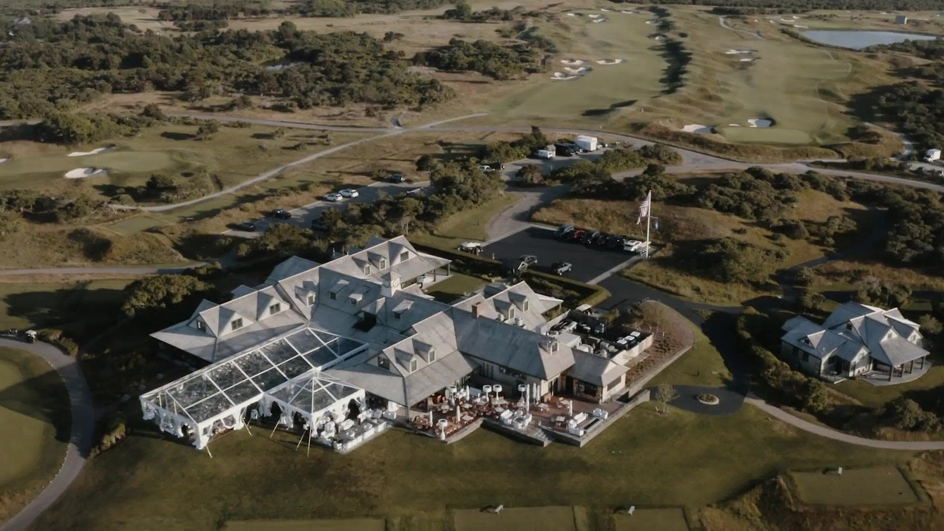 An aerial view of the Nantucket Golf Club clubhouse with a clear-top tent on its terrace and the course beyond