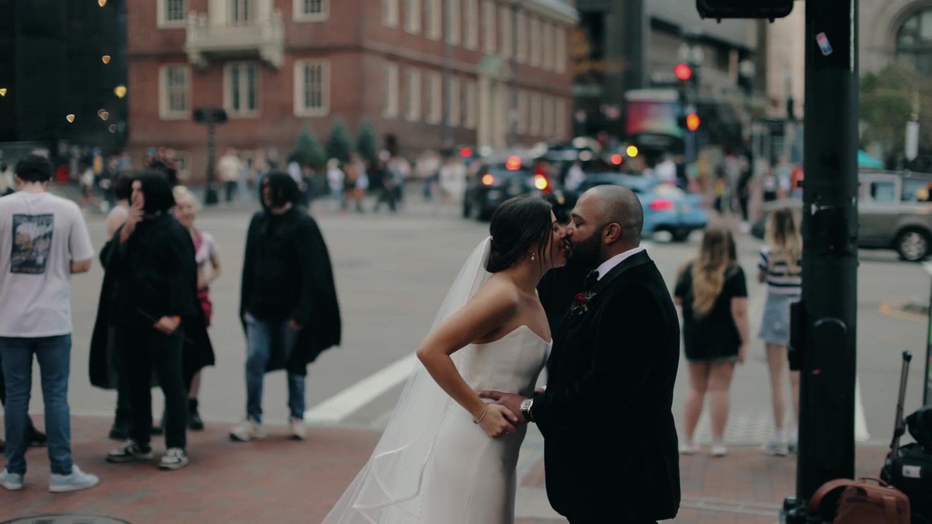 A bride and groom kissing on a street corner in downtown Boston with the Old State House behind them