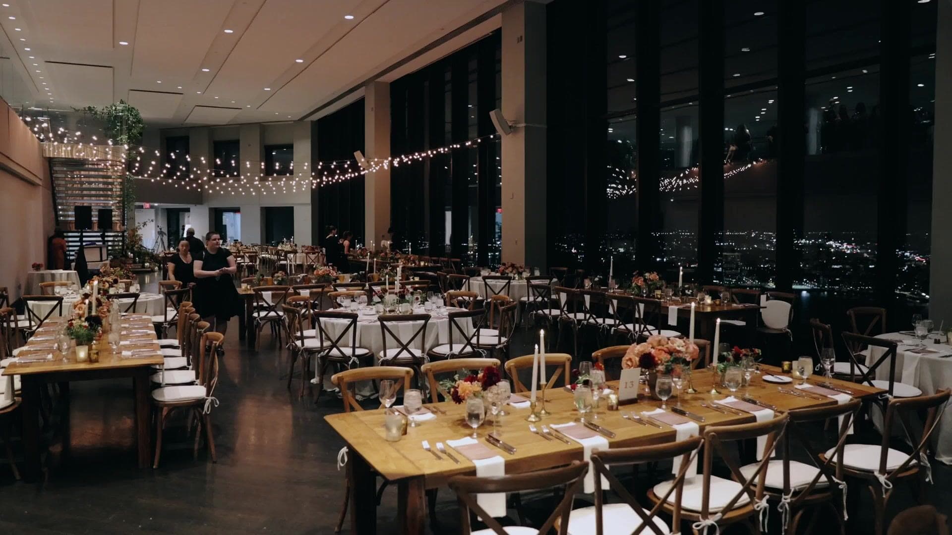 The State Room set for dinner, with long wooden tables under strings of bistro lights and the city lit up in the windows